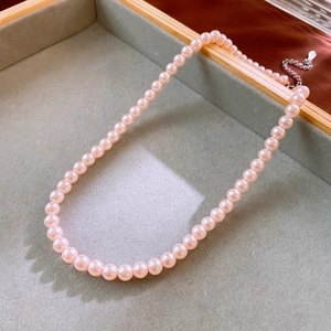 Close-up of pink pearl necklace with silver adjustable chain on a grey velvet tray