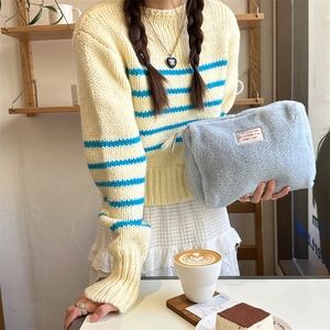 Woman holding a large light blue faux shearling toiletry bag in a cozy cafe setting