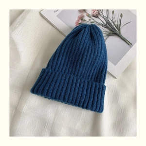 Close-up of deep blue knitted beanie with rolled edge texture on a minimalist background