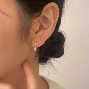 Detail of gold bow earrings with a teardrop crystal pendant worn by a model