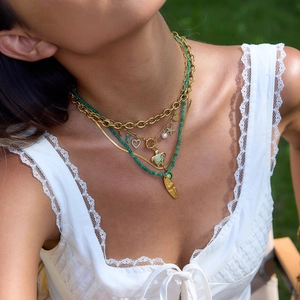 Layered gold necklace set with green beads, shell and turtle charms on a model