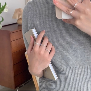 Silver bow and wavy stackable minimalist rings worn by model in a cozy home setting