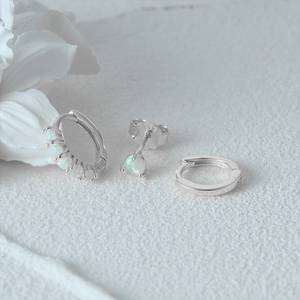 Close-up of S925 sterling silver evil eye earrings set with opal stones on white fabric