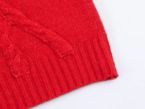 Detailed close-up of red cable knit sweater featuring thick texture and ribbed hem detail
