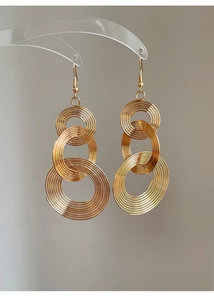 Macro detail of triple hollow spiral gold earrings hanging on a transparent curved stand