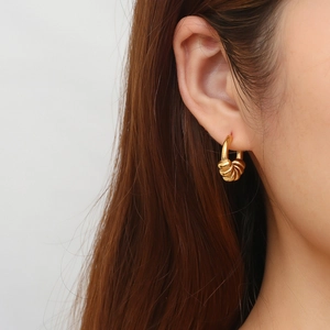 Close-up of gold spiral twisted C-shape hoop earrings worn on ear for women