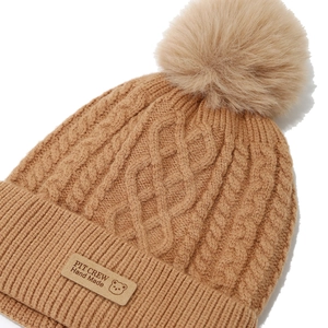 Detailed knit pattern of brown beanie with faux fur pompom and leather bear patch