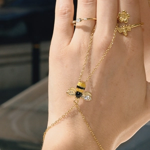 Makro-Detail eines goldenen Bienen-Armbands mit Emaille und Kristallen an der Hand