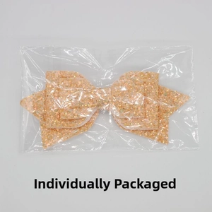 Close-up of glittery peach bow straw accessory and elastic band in individual packaging