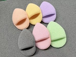 Detailed view of six colorful teardrop cleansing sponges with finger pockets on a grey mat