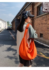 Detail of a vibrant orange hobo crossbody bag featuring a wide ergonomic shoulder strap
