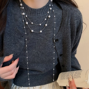 Makro-Detail der mehrlagigen Perlen-Quastenkette auf einem grauen Strickpullover