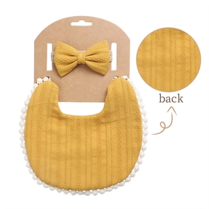 Detail of ginger cotton baby bib with pom-pom lace edge and matching bow headband