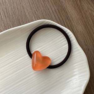 Close-up of translucent orange-pink heart pendant on a black elastic hair band