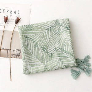 Close-up of green palm leaf pattern on lightweight scarf with decorative tassels