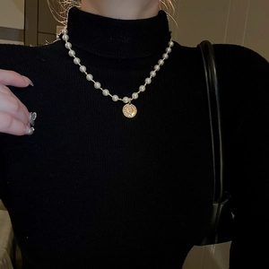 Detailansicht der Perlenkette mit Goldmünzen-Porträtanhänger auf schwarzem Pullover