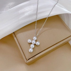 Detailed close-up of pearl cross pendant on silver chain over silk background