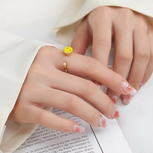 Detail of adjustable gold ring featuring a yellow smiley face and white pearl on finger