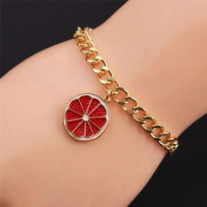 Detail of gold chain bracelet featuring a colorful grapefruit enamel fruit charm on wrist