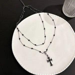 Dettaglio della collana a doppia croce gotica con pietre nere e catena con perline
