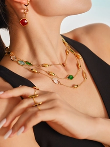 Close-up of layered gold chain necklace with green glass charms and matching jewelry set