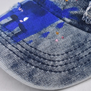 Close-up of distressed washed denim baseball cap with paint splatter and frayed brim detail