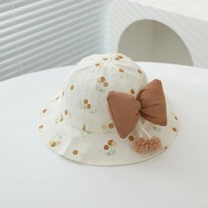 Detail of baby sun hat with fruit print, large brown bow and decorative pom poms