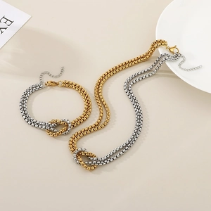 Detail of mixed-metal intertwined necklace and bracelet set in gold and silver finish