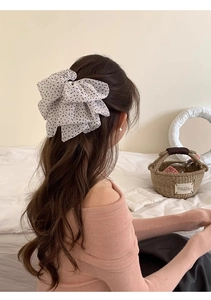 Close-up of a large white chiffon hair bow with black polka dots on a woman's ponytail