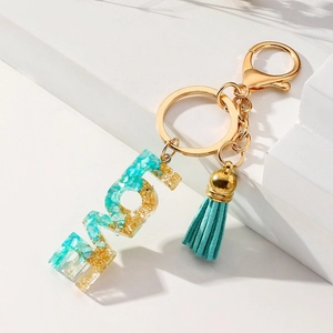 Detail of resin MOM keychain with gold foil, green stone inlay and suede tassel