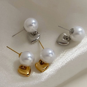 Elegante Herz-Perlenohrringe in Gold und Silber auf einem weichen Hintergrund aus Seide