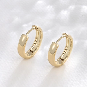Dettaglio di orecchini a cerchio placcati oro lucido con finitura liscia minimalista