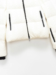 Detail of white cable knit puffer jacket featuring black zippers and windproof cuffs