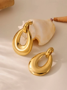 Detailed close-up of large golden teardrop earrings on a minimalist natural background