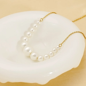 Elegant gold pearl necklace with graduated white pearls displayed on a white ceramic tray