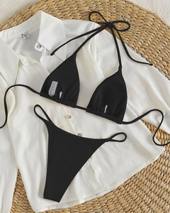 Detailed flat lay of black ribbed bikini set with halter top on white shirt and straw mat
