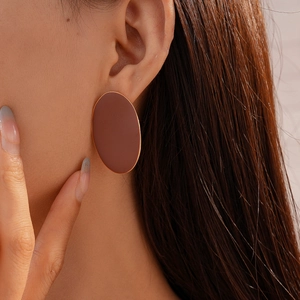 Close-up of a model wearing brown oval matte earrings with gold metallic edge accents