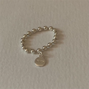 Minimalist 925 sterling silver beaded ring with round tag charm on ivory textured background