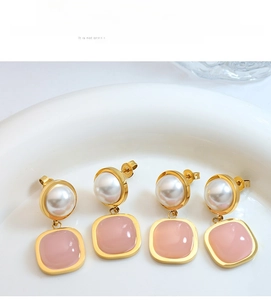 Detail of pink stone and pearl drop earrings with golden metal frames in a ceramic tray