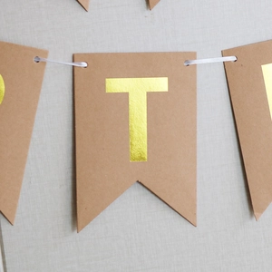 Detail of kraft paper party banner featuring gold foil letter T on a fishtail pennant