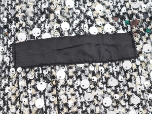 Detail of tweed fabric with silver sequins and black satin trim on a sleeveless dress