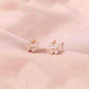 Macro shot of gold four-leaf clover earrings with zircon hearts on pink silk