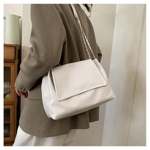 Close-up of a white glossy leather shoulder bag with a silver woven chain strap on a model
