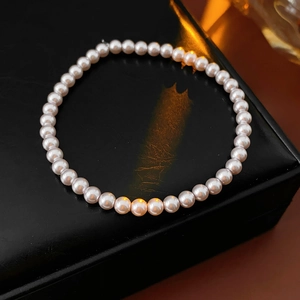 Macro detail of elegant pink pearl bracelet on black leather surface with warm lighting