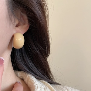 Detailed view of cream acrylic C-shaped stud earrings worn on ear with minimalist style