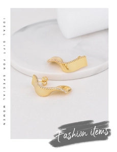 Detailed view of gold wave earrings with white cubic zirconia on a marble surface