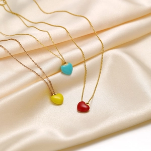 Three gold necklaces with red, yellow, and blue heart pendants on silk fabric