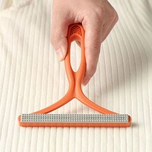 Orange manual lint remover for pet hair cleaning on a beige knitted sweater fabric