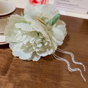 Detail of light green floral hair claw with sparkling rhinestone tassels on wooden table