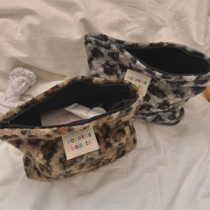 Detail of plush leopard print makeup bag with zipper closure and logo tag on fabric